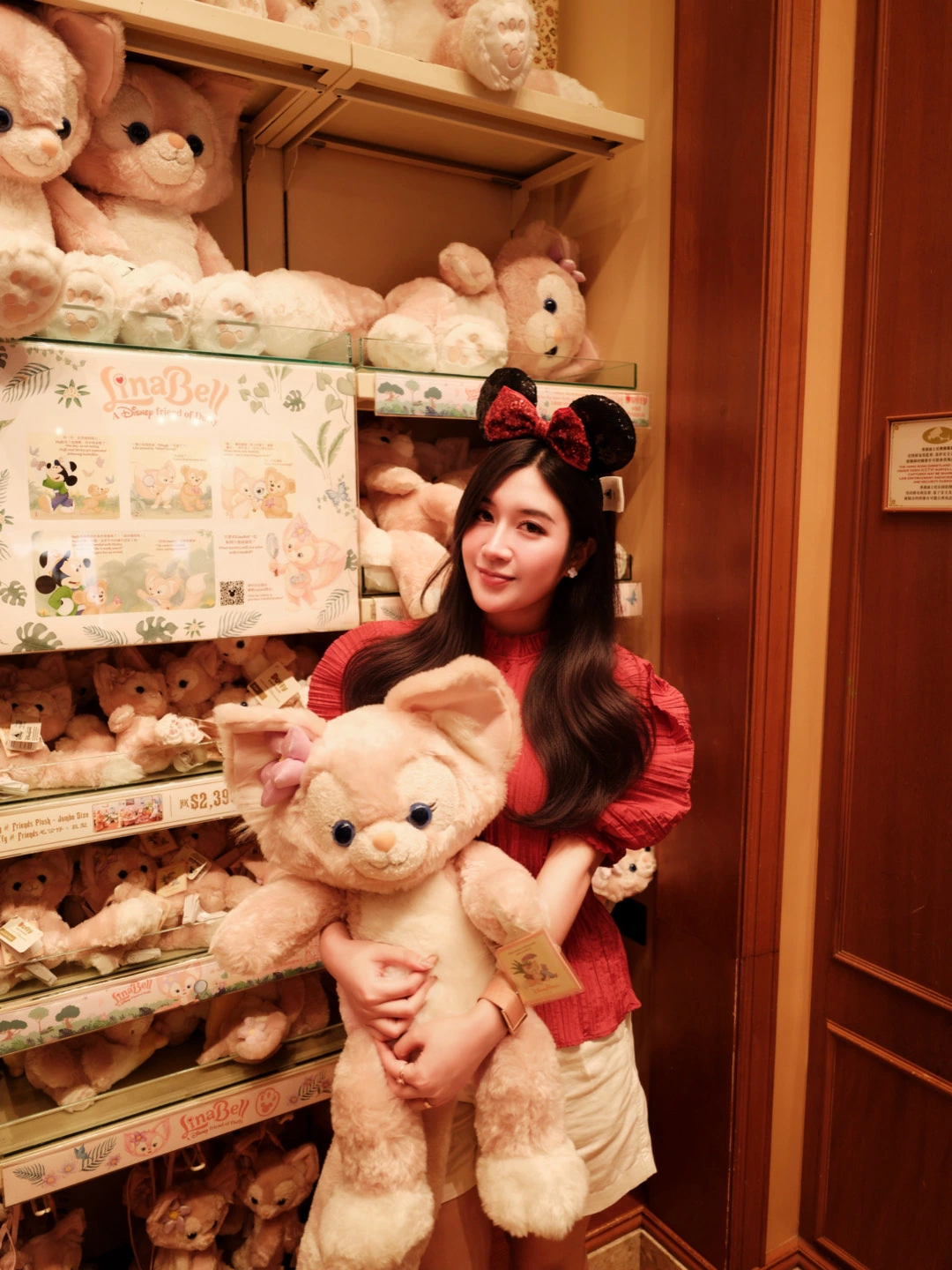 A woman smiling at the camera while hugging a large plush rabbit in a toy shop.