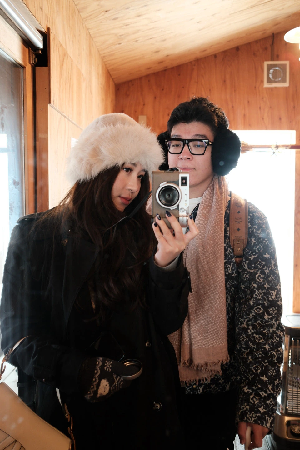 The couple taking a mirror selfie in winter hats, earmuffs, and a scarf.