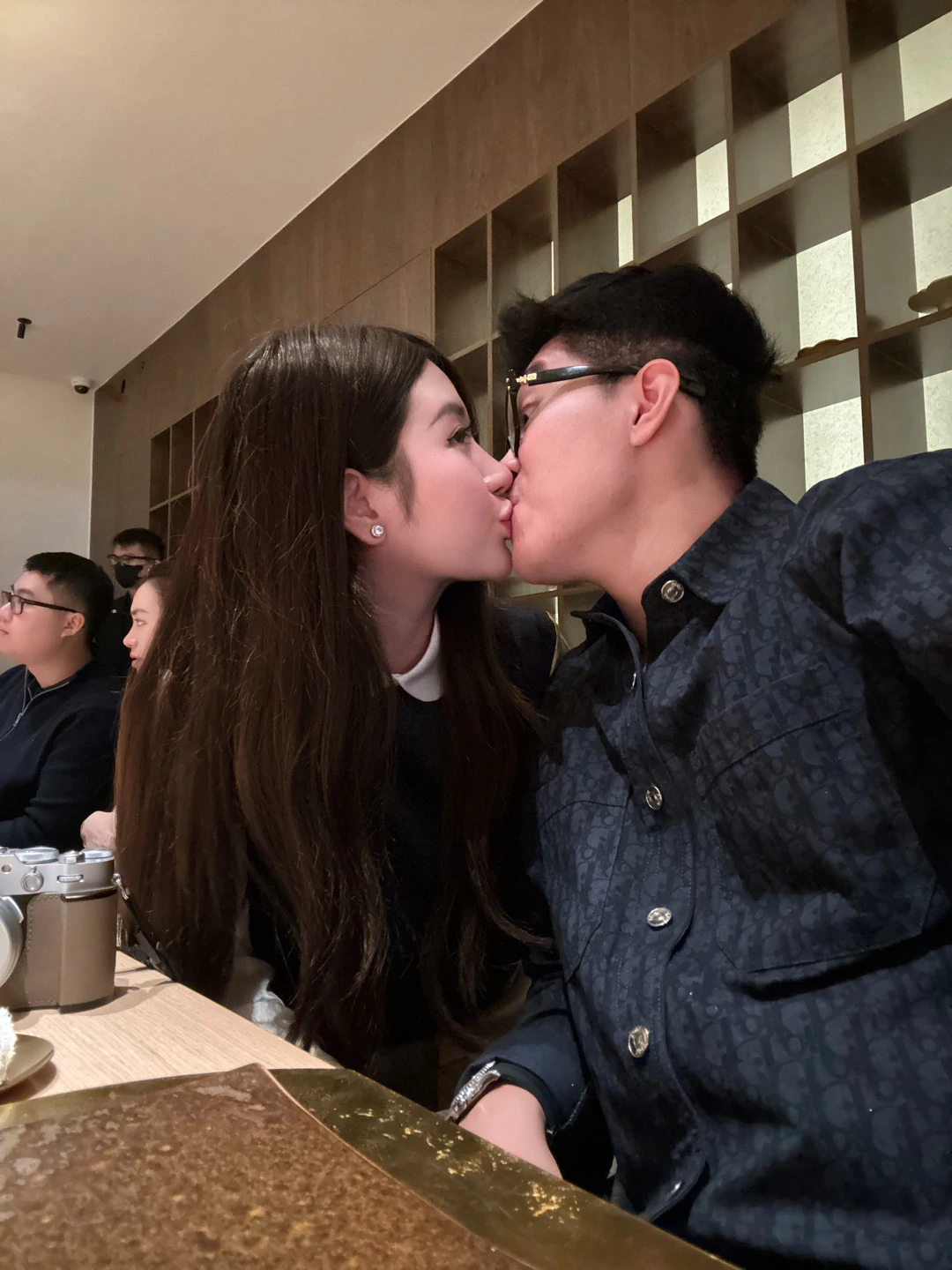 The couple sharing a kiss while seated together at a restaurant table.